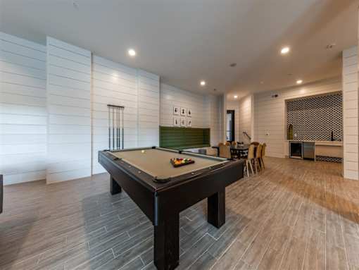 A billiards table near a seating area with a table, 8 chairs, and a wet bar in a clubhouse.