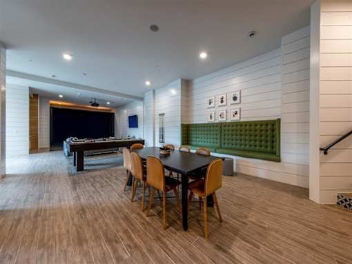 A community room with  a table, 8 chairs, a build-in seating area, and a billiards table.
