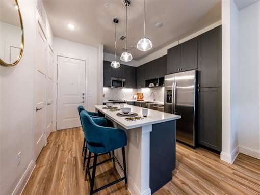 A kitchen with an island, stainless steel appliances, hardwood-style flooring and pendant lights.