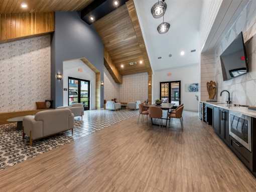 A clubhouse with vaulted ceilings, three seating areas with chairs and tables, and a wet bar with a TV.