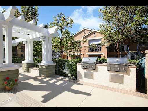 A white pergola is in the middle of a patio with two grills on the wall.