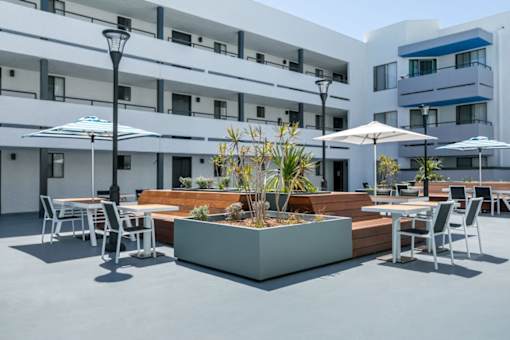 a patio with tables and chairs and umbrellas in front of a building at Harbor Terrace Apartments, San Pedro , CA 90731
