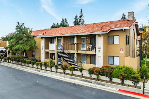 A building with a red roof and beige walls with a staircase leading to the entrance.