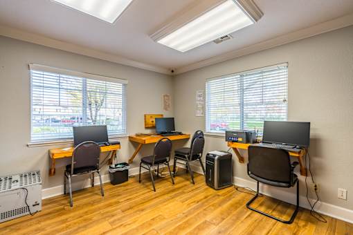 A room with a desk, chairs, and computers.