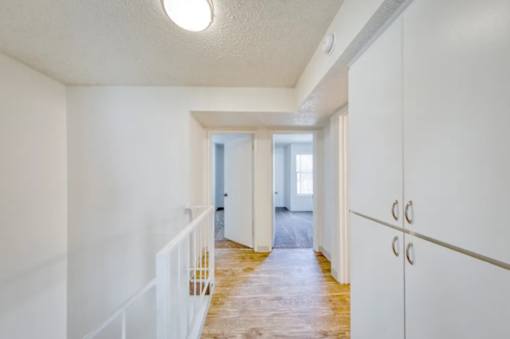 A long hallway with a white railing on the left and a white door on the right.