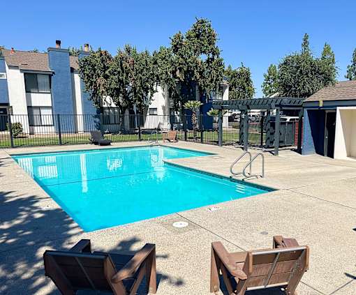 A swimming pool surrounded by chairs and trees.
