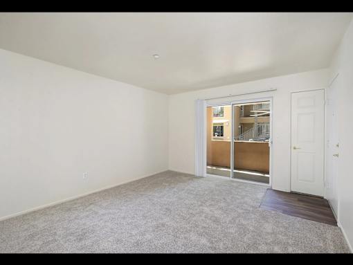 A room with a carpeted floor and a sliding glass door leading to another room.