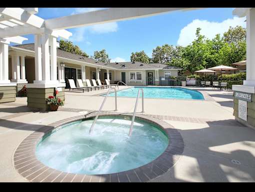 A hot tub sits in the middle of a pool surrounded by a white pergola.