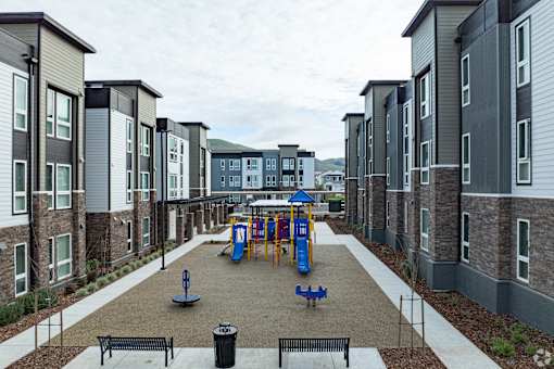 A playground area with a slide and swings is surrounded by apartment buildings.