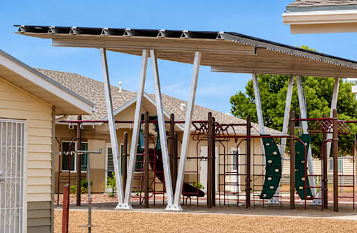 A playground with a slide and swings under a canopy.