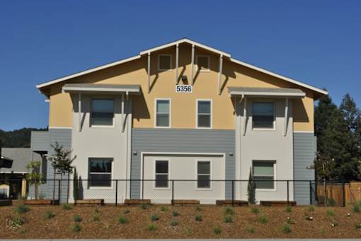 A two-story house with a grey and beige exterior and a black fence in front.