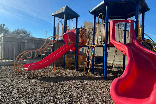 A playground with a red slide and a blue roofed structure.
