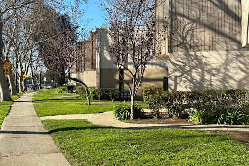 A sidewalk runs alongside a grassy area in front of a building.