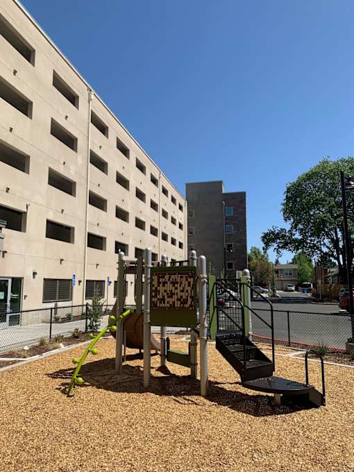 A playground with a slide and a climbing frame in front of a building.