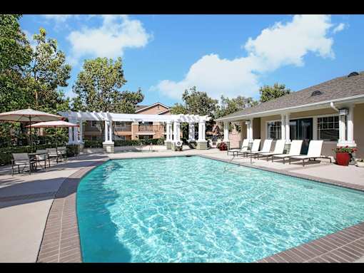 A pool surrounded by a patio with chairs and umbrellas.