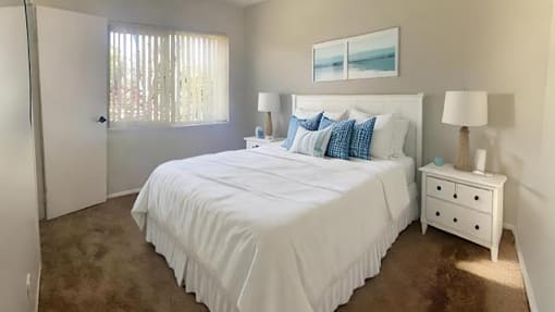 A bedroom with a large bed, a nightstand, and a window with curtains.