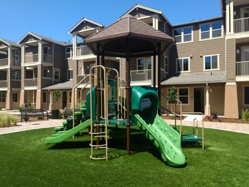 a playground with a gazebo and slides in front of an apartment complex