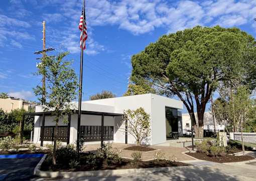 A white building with a black door and windows is surrounded by trees and plants.