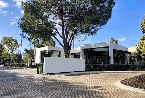 A modern house with a white fence and a large tree in front.