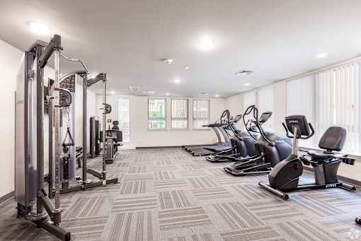 A well-lit gym with a variety of equipment including treadmills, stationary bikes, and weight machines.