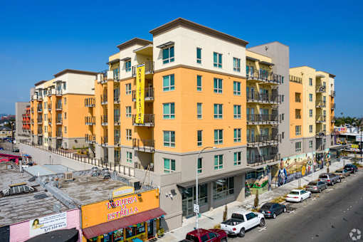 A street view of a yellow and white apartment building with cars parked in front.