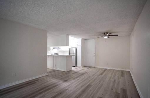 an empty living room with white walls and a kitchen at The Arbors Santa Ana, California, 92705