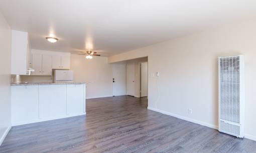 an empty living room and kitchen with white walls and wood flooring