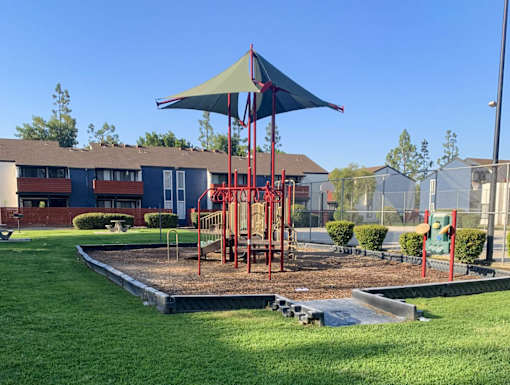 A playground with a red swing set and a blue umbrella.