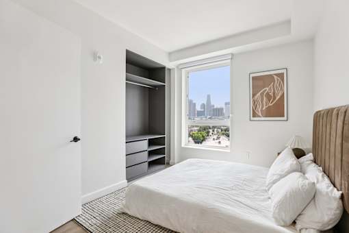 A bedroom with a large bed and a city view through the window.
