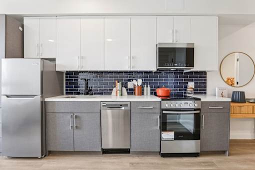 A modern kitchen with stainless steel appliances and a grey backsplash.