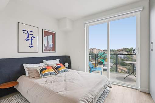 A bedroom with a bed, a bench, and a window overlooking a balcony.