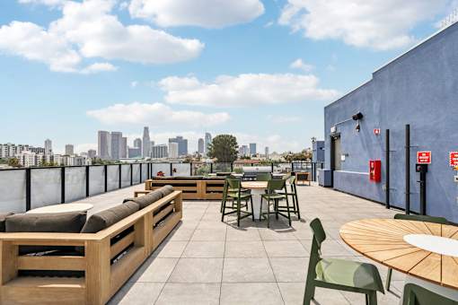 A rooftop patio with wooden furniture and a city skyline in the background.