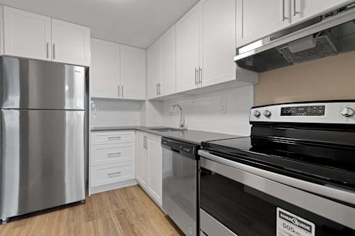 A kitchen with a stainless steel refrigerator, a stove, and white cabinets.