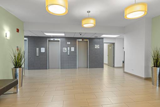 A hallway with tiled floors, grey doors, and yellow ceiling lights.