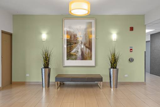 A hallway with a bench, two potted plants, and a framed picture on the wall.
