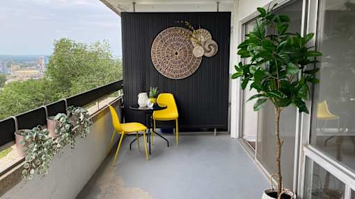 A balcony with a table and chairs and a potted plant.