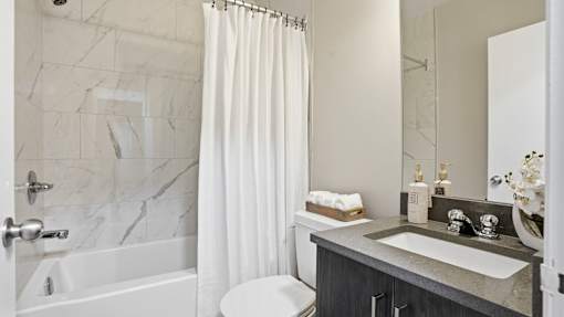 A bathroom with a marble patterned tub and a white shower curtain.
