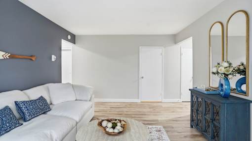 A white couch with blue pillows sits in a room with a wooden floor and a mirror on the wall.