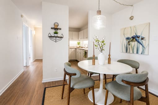 A white dining table with four grey chairs and a vase of flowers on it.