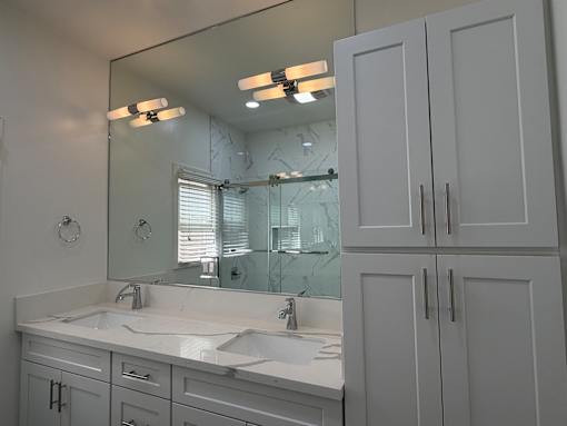 A bathroom with a large mirror, two sinks, and white cabinets.