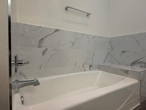 A white bathtub with a silver faucet and a marble tile wall.