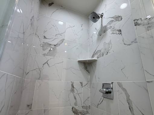 A shower area with a marble tile wall and a shower head.