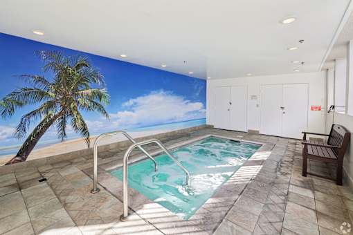 A wall mural of a beach scene is behind a small indoor pool.