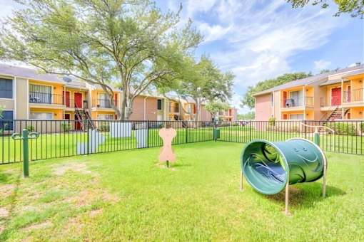 A playground with a green slide and a pink teddy bear in the middle of a grassy area.