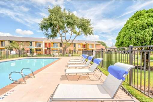 A sunny day at the pool with lounge chairs and a fence.
