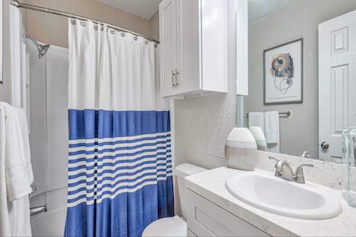 A white and blue bathroom with a white sink and a blue shower curtain.