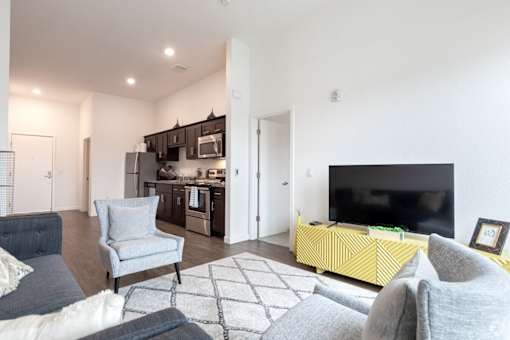 A modern living room with a grey sofa, a grey armchair, a yellow ottoman, and a black television.
