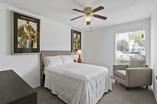 A bedroom with a bed, chair, and two paintings on the wall.