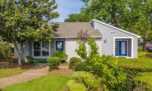 A small house with a blue door is surrounded by greenery.