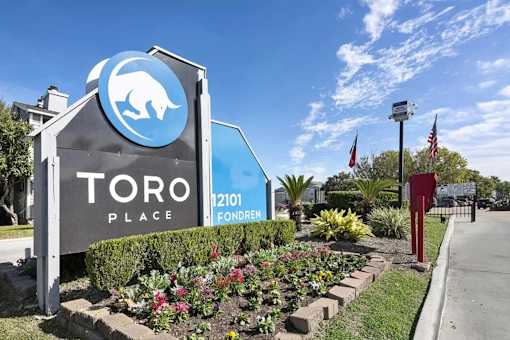 A sign for Toro Place with a blue bear logo and a red pole with an American flag.